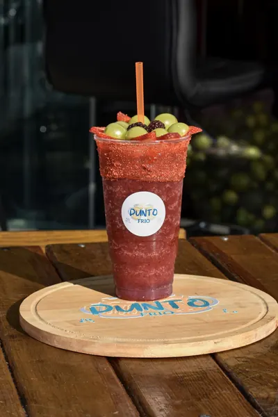Bebida roja escarchada con fruta sobre tabla con el logo de Punto Frío